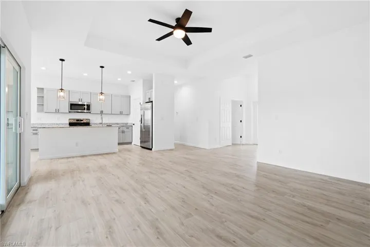 Unfurnished living room featuring ceiling fan, a raised ceiling, light hardwood / wood-style flooring, and sink