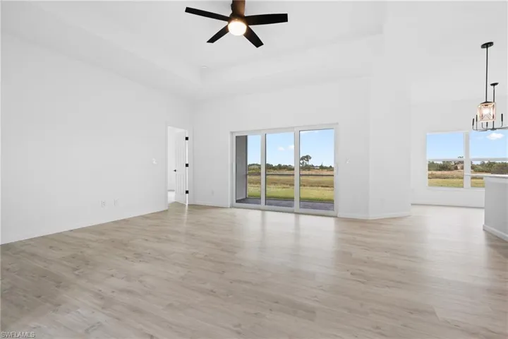 Unfurnished living room featuring a towering ceiling, ceiling fan with notable chandelier, plenty of natural light, and light hardwood / wood-style flooring