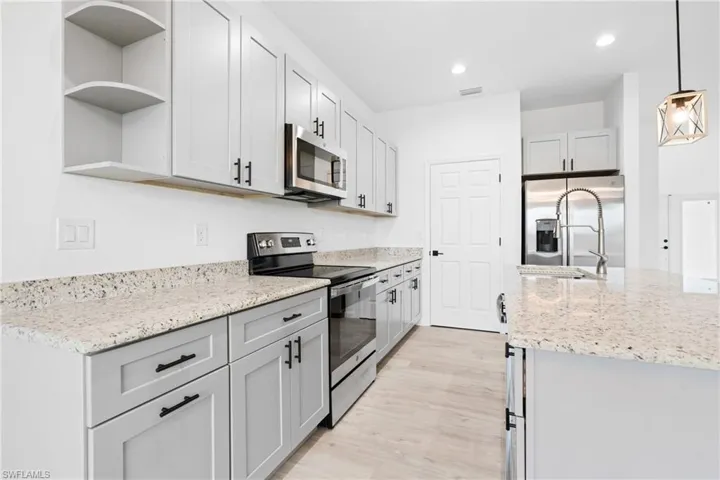 Kitchen with light stone countertops, appliances with stainless steel finishes, hanging light fixtures, and light hardwood / wood-style flooring