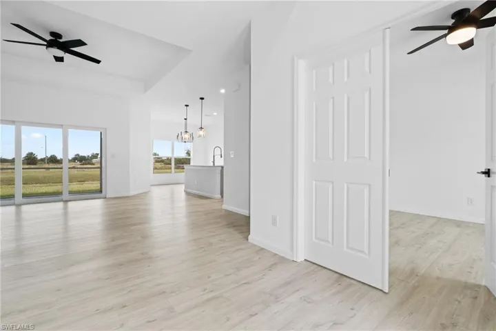 Unfurnished living room with sink, light hardwood / wood-style floors, and ceiling fan with notable chandelier