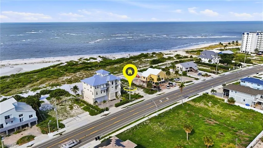 Elevated coastal home featuring multiple balconies, a light blue metal roof, and direct beach proximity - Virtually Edited Image