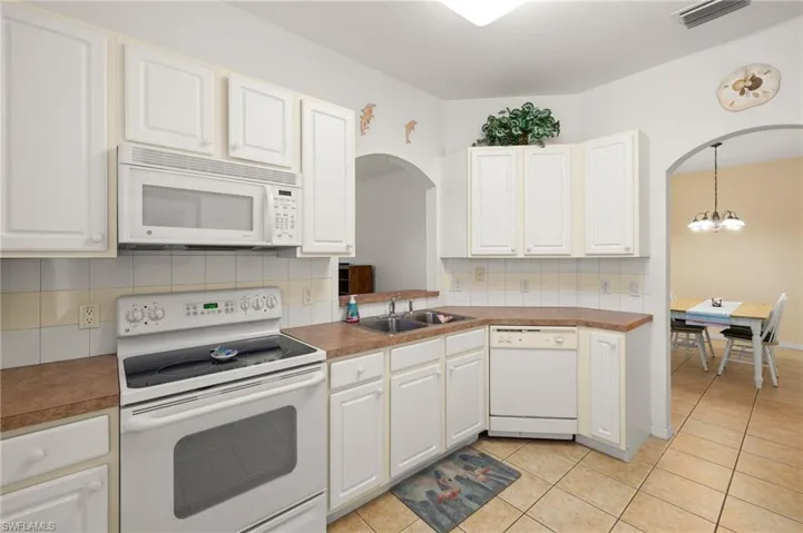 Kitchen featuring sink, white appliances, tasteful backsplash, white cabinets, and light tile patterned flooring