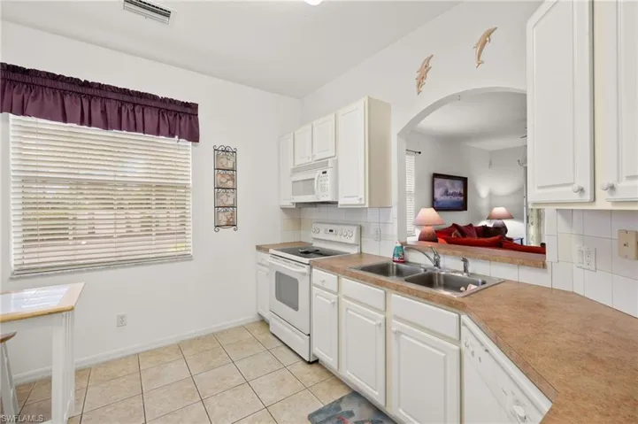 Kitchen featuring sink, white appliances, light tile patterned floors, white cabinetry, and tasteful backsplash