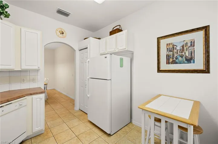 Kitchen with white cabinetry, light tile patterned floors, backsplash, and white appliances