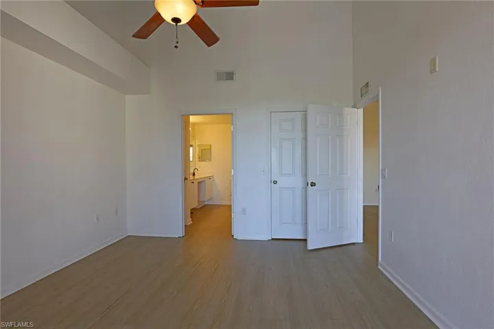 Unfurnished bedroom featuring wood finished floors, ensuite bathroom, a high ceiling, and ceiling fan