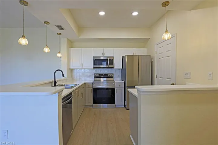 Kitchen featuring a peninsula, pendant lighting, stainless steel appliances, light countertops, and tasteful backsplash