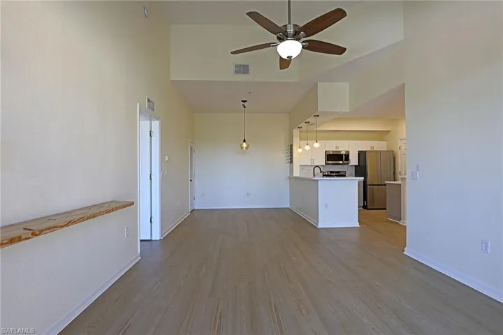 Unfurnished living room featuring dark wood-style floors, a ceiling fan, and a high ceiling