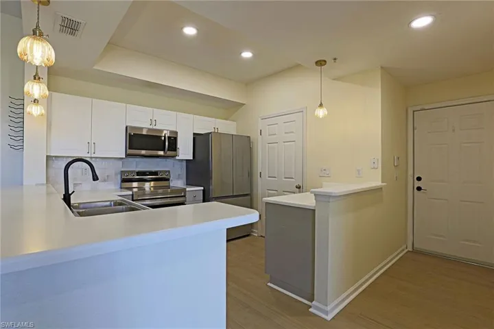 Kitchen with pendant lighting, a peninsula, stainless steel appliances, decorative backsplash, and light countertops