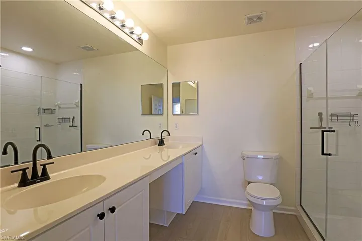 Full bath featuring a stall shower, double vanity, and light wood-type flooring