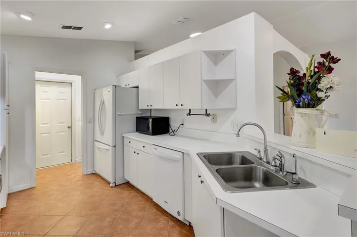 White laminate kitchen cabinets with ample cabinet space and tile floor. View of refrigerator.