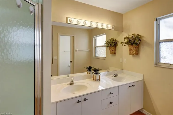 Master Bathroom with white cabinets and double sinks. Window has hurricane covers.