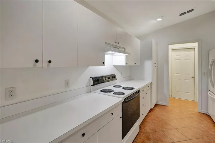 View of white Kitchen cabinets, stove and laundry room entry way.