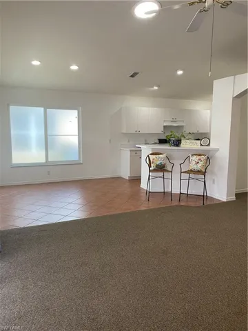 Kitchen with kitchen peninsula, a kitchen breakfast bar, white cabinetry, light tile floors, and range hood
