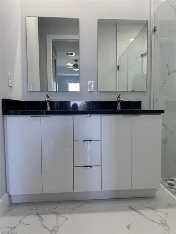 Full bathroom with double vanity, marble finish floor, a marble finish shower, and ceiling fan