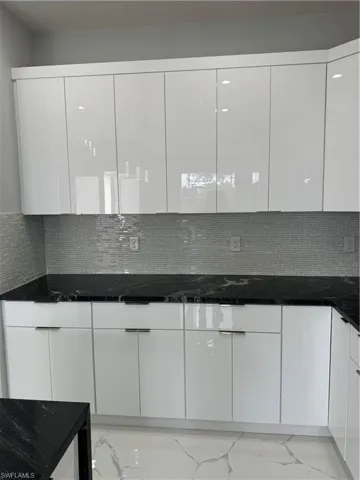 Kitchen with white cabinetry, tasteful backsplash, and dark stone counters