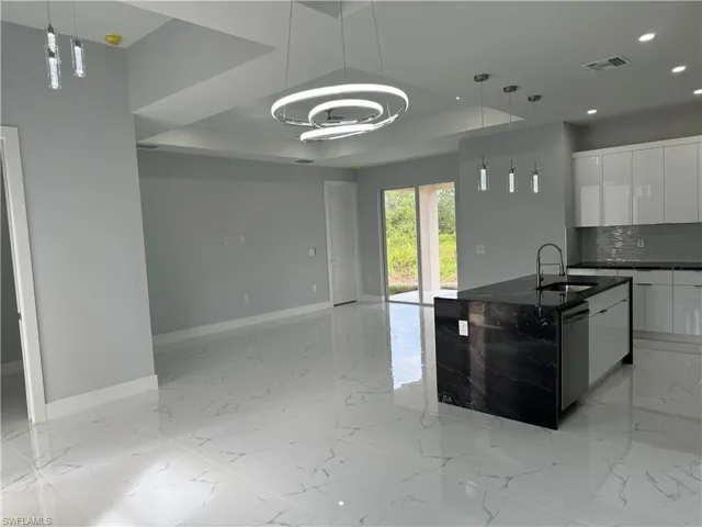 Kitchen featuring sink, white cabinetry, decorative light fixtures, stainless steel dishwasher, and decorative backsplash