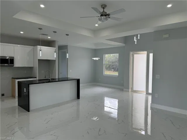 Kitchen with decorative backsplash, white cabinets, a center island with sink, decorative light fixtures, and sink