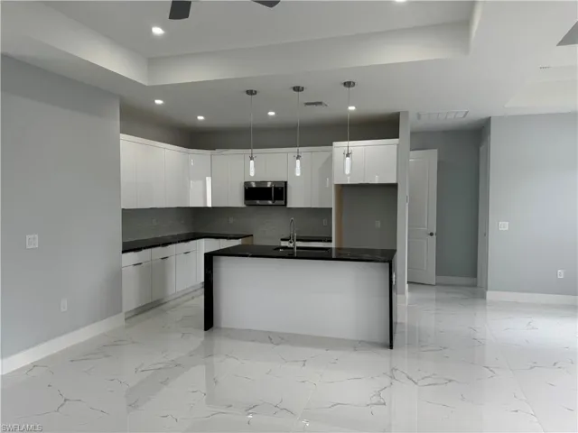 Kitchen with a kitchen island with sink, a tray ceiling, backsplash, decorative light fixtures, and white cabinetry