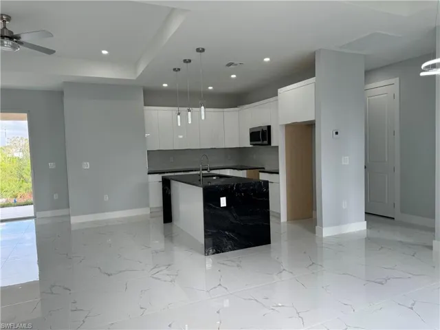 Kitchen featuring white cabinets, tasteful backsplash, a kitchen island with sink, pendant lighting, and sink
