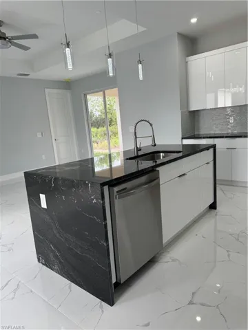 Kitchen with sink, pendant lighting, stainless steel dishwasher, white cabinets, and a center island with sink