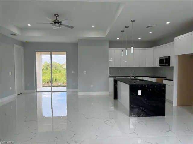 Kitchen featuring decorative backsplash, white cabinets, hanging light fixtures, a center island with sink, and a raised ceiling