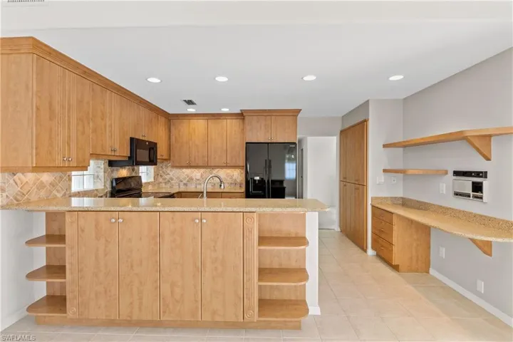Kitchen featuring light tile patterned floors, kitchen peninsula, backsplash, light stone counters, and black appliances