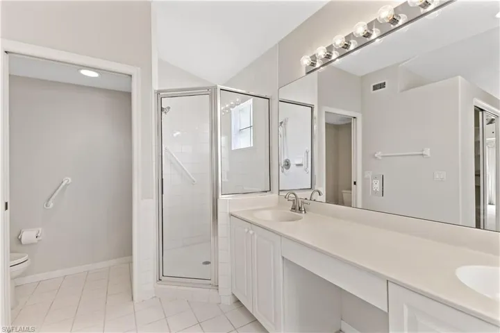 Bathroom featuring tile patterned flooring, a shower with door, toilet, and dual bowl vanity