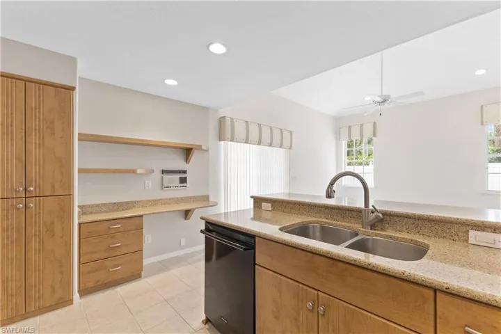 Kitchen with black dishwasher, sink, light stone counters, light tile patterned flooring, and ceiling fan