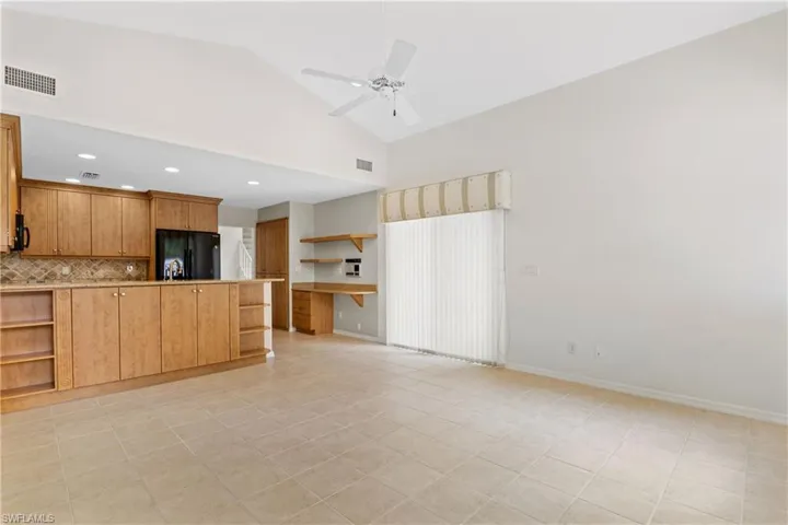 Kitchen featuring light tile patterned flooring, ceiling fan, black refrigerator, high vaulted ceiling, and backsplash
