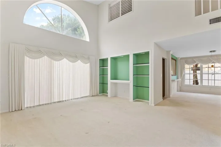 Empty room featuring plenty of natural light, a high ceiling, and light carpet