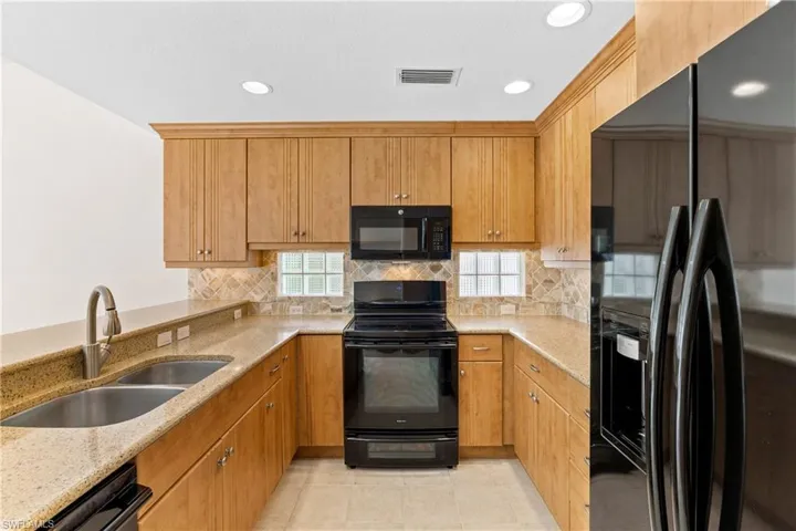 Kitchen featuring black appliances, tasteful backsplash, sink, light stone counters, and light tile patterned floors
