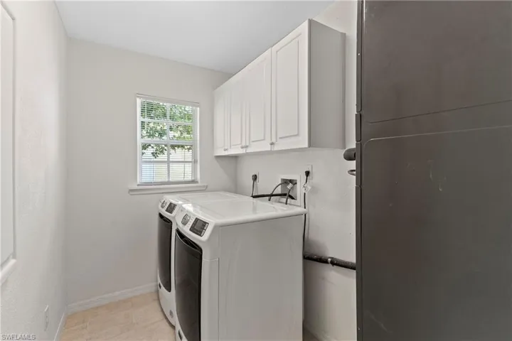 Laundry area with light tile patterned flooring, cabinets, and washing machine and clothes dryer