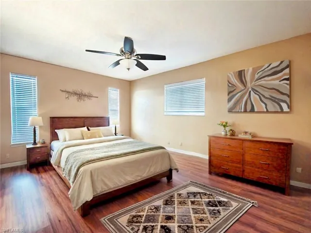 Bedroom featuring a ceiling fan, baseboards, multiple windows, and wood finished floors