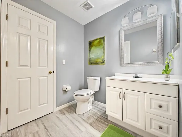 Half bath featuring baseboards, vanity, toilet, and visible vents