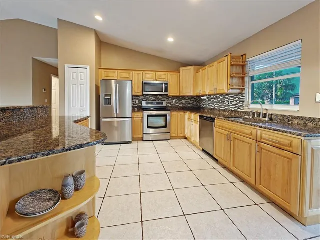 Kitchen with open shelves, decorative backsplash, a sink, vaulted ceiling, and stainless steel appliances