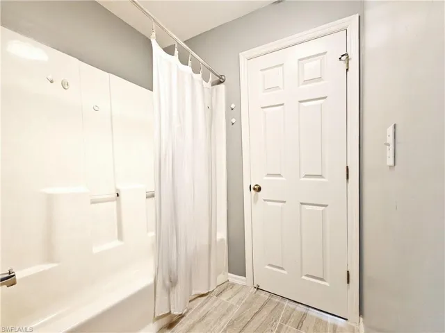 Bathroom with baseboards, wood finished floors, and shower / tub combo with curtain