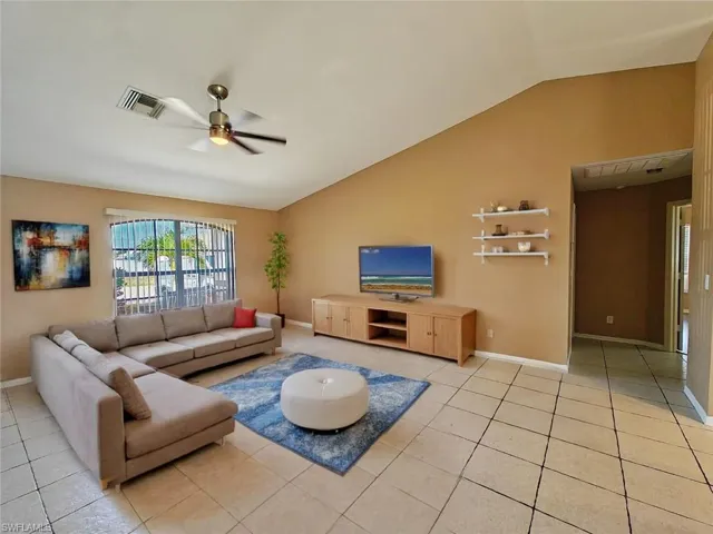 Living area featuring a ceiling fan, visible vents, light tile patterned floors, and vaulted ceiling