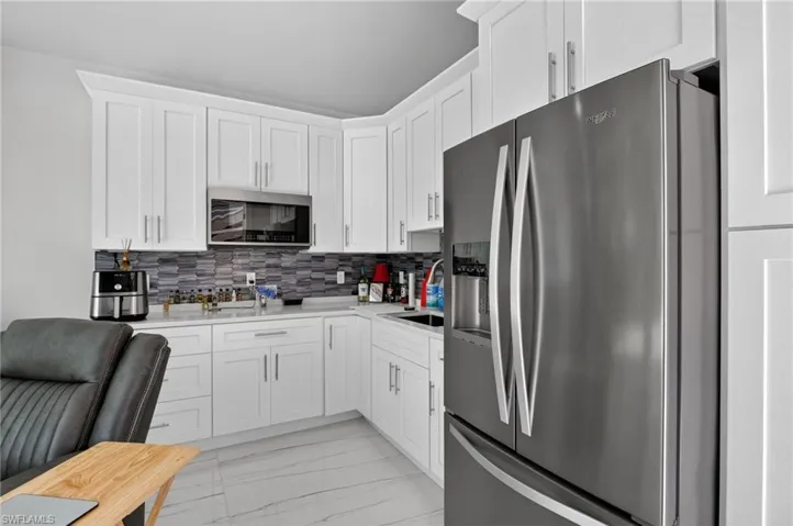 Kitchen featuring stainless steel appliances, white cabinetry, light marble finish floors, backsplash, and light stone countertops