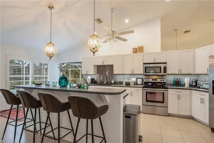 Kitchen featuring appliances with stainless steel finishes, light tile patterned floors, dark countertops, high vaulted ceiling, and backsplash