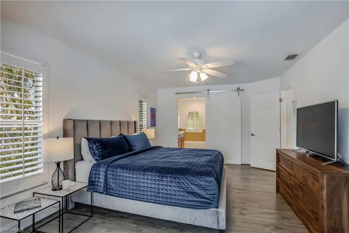 Bedroom with a barn door, wood finished floors, a ceiling fan, and ensuite bathroom