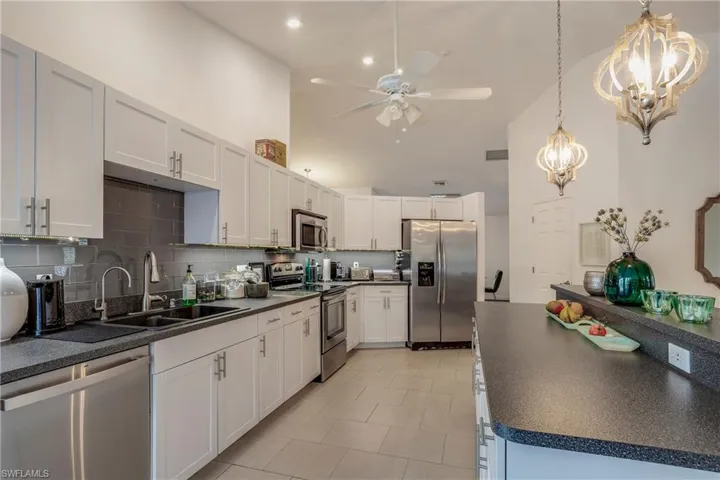 Kitchen featuring stainless steel appliances, dark countertops, a chandelier, ceiling fan, and a high ceiling