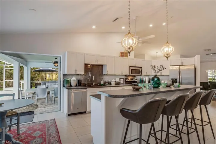 Kitchen with stainless steel appliances, ceiling fan, dark countertops, high vaulted ceiling, and decorative backsplash