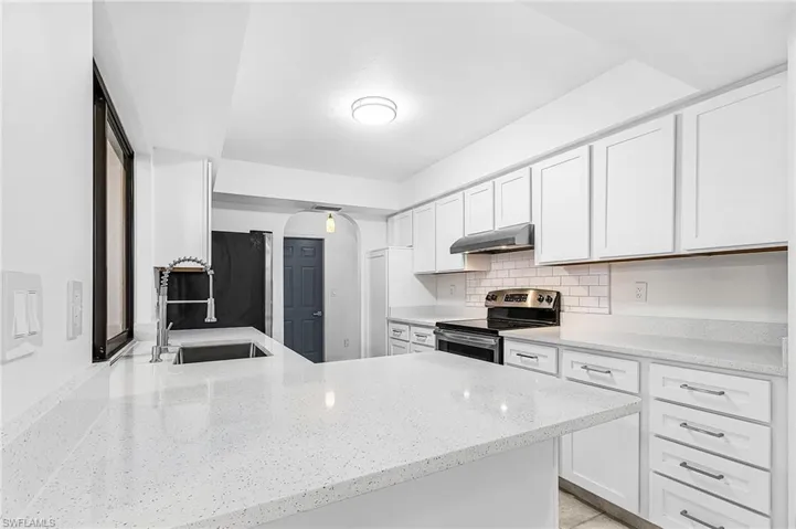 Kitchen featuring white shaker-style cabinetry, light-toned countertops, subway tile backsplash, stainless steel sink, and modern pull-down faucet
