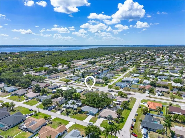 Suburban neighborhood featuring a variety of single-story residential properties, mature trees, and a visible waterway in the background