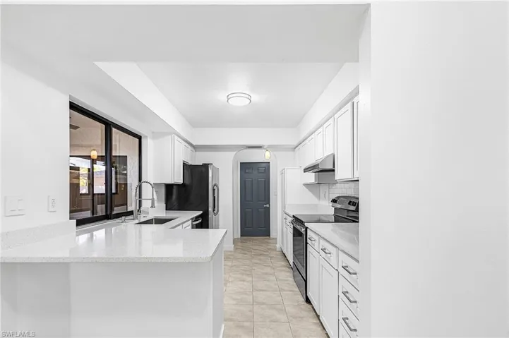 Kitchen featuring white cabinetry, light-toned countertops, a stainless steel sink with a gooseneck faucet, black appliances, and tiled flooring