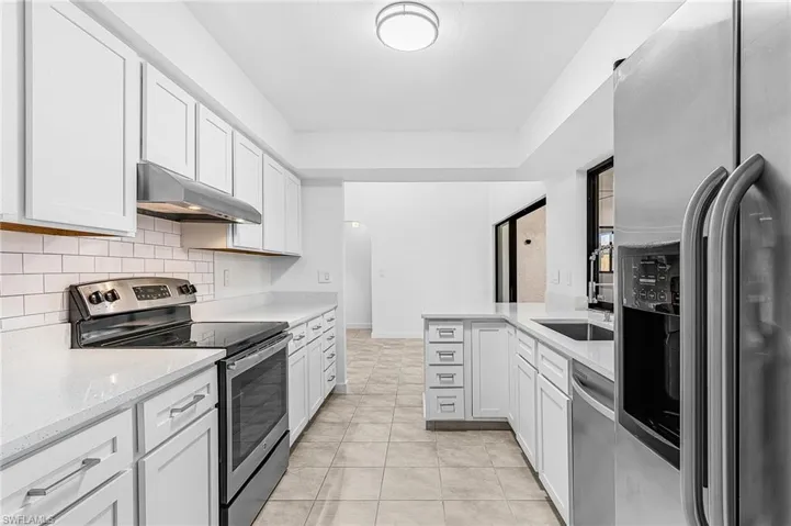 Modern kitchen featuring white shaker cabinetry, light-toned countertops, subway tile backsplash, stainless steel appliances, and tile flooring