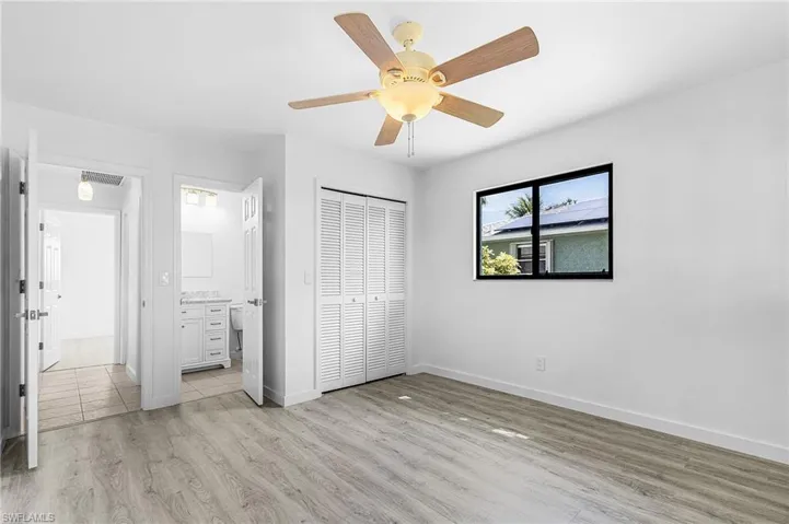 Spacious room featuring wood-finish flooring, a ceiling fan with light fixture, and a large window with black trim