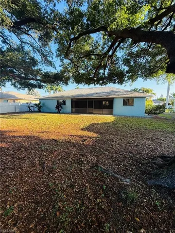 Expansive backyard featuring a mature tree canopy, screened-in patio, light blue exterior siding, and a shingled roof