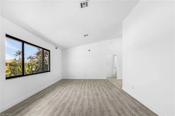 Spacious interior with wood-finish flooring, a contemporary black-framed window, bright white walls, and a recessed arched doorway