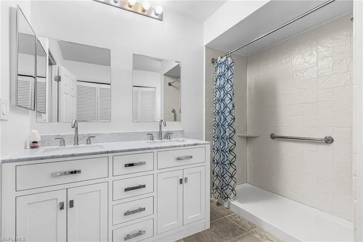 Bathroom featuring a double vanity with white cabinetry, a light-toned countertop, and dual sinks with chrome fixtures